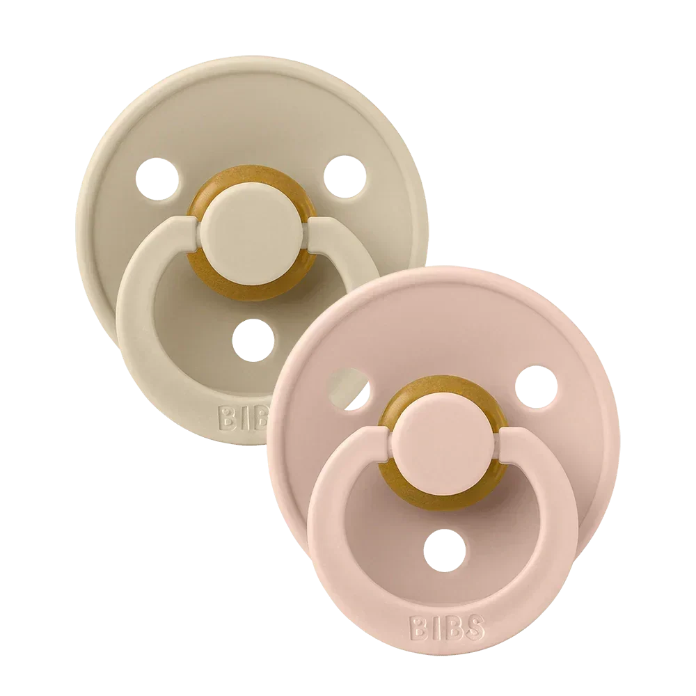 Two round latex baby pacifiers, blush pink and vanilla beige with gold accents