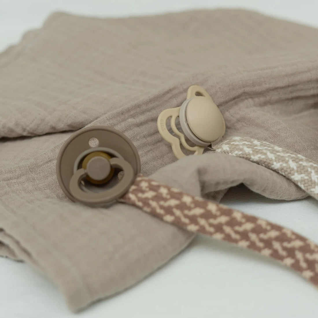 Woven pacifier clip with blush-and-ivory strap, BIBS tag, and metal clasp