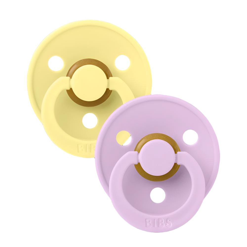 Two silicone pacifiers: one yellow and one lavender, round shield with ventilation holes