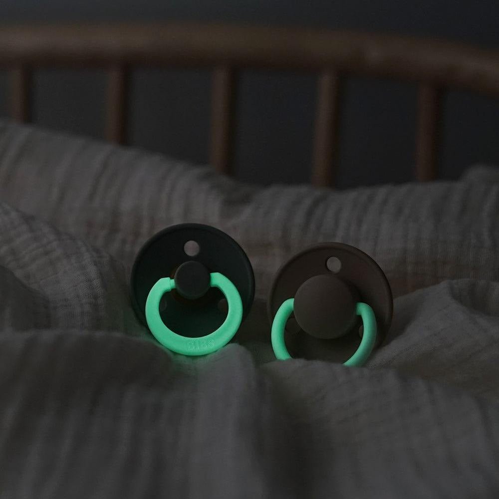Two pacifiers with dark shields and glowing green rim around the nipple guard